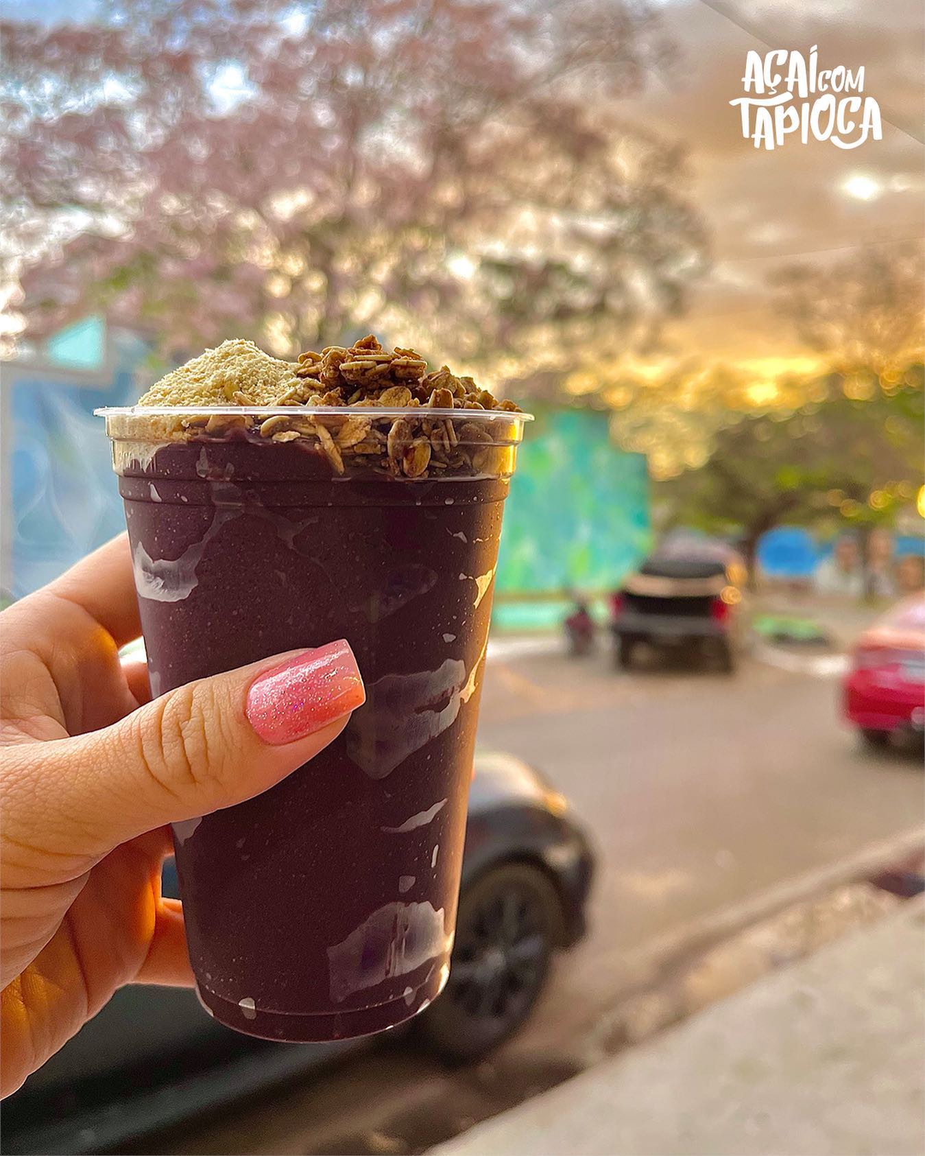 Copo de açaí com granola e leite em pó no topo, segurado na mão