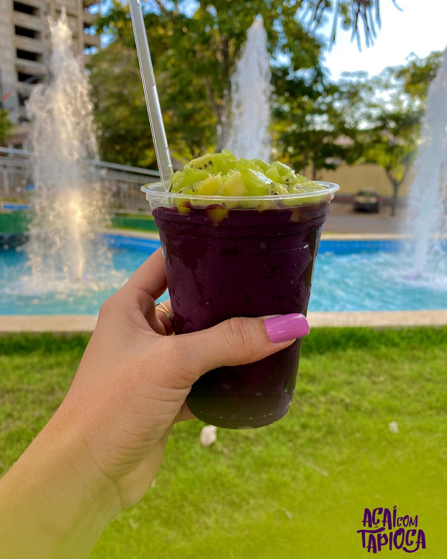 Açaí com pedaços de kiwi por cima, ao ar livre perto de uma fonte