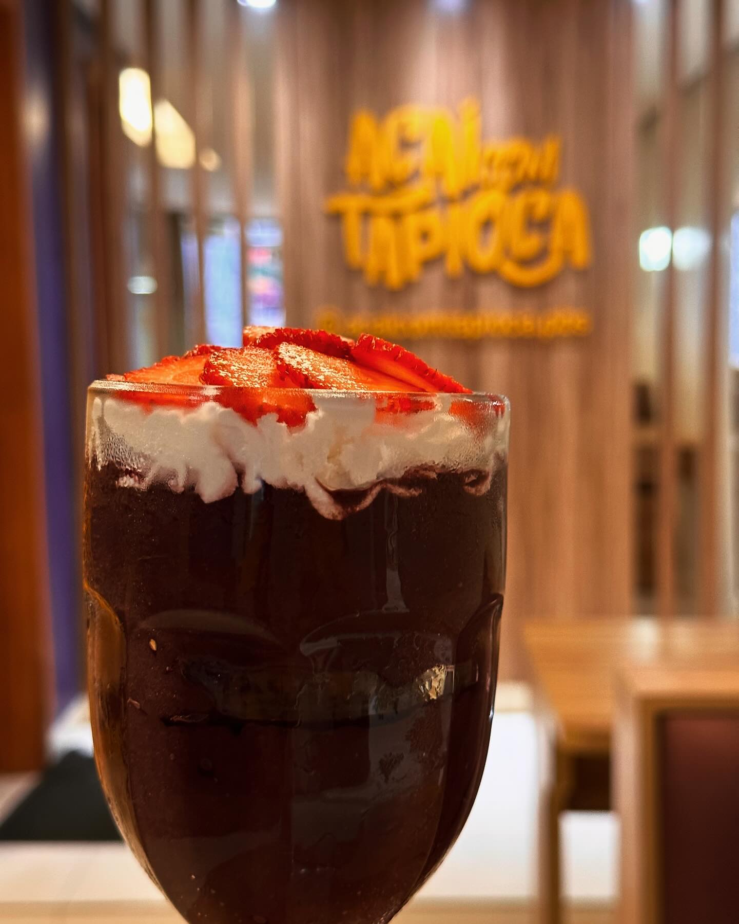 Copo alto de açaí cremoso com chantilly e fatias de morango no topo, na loja da Açaí com Tapioca
