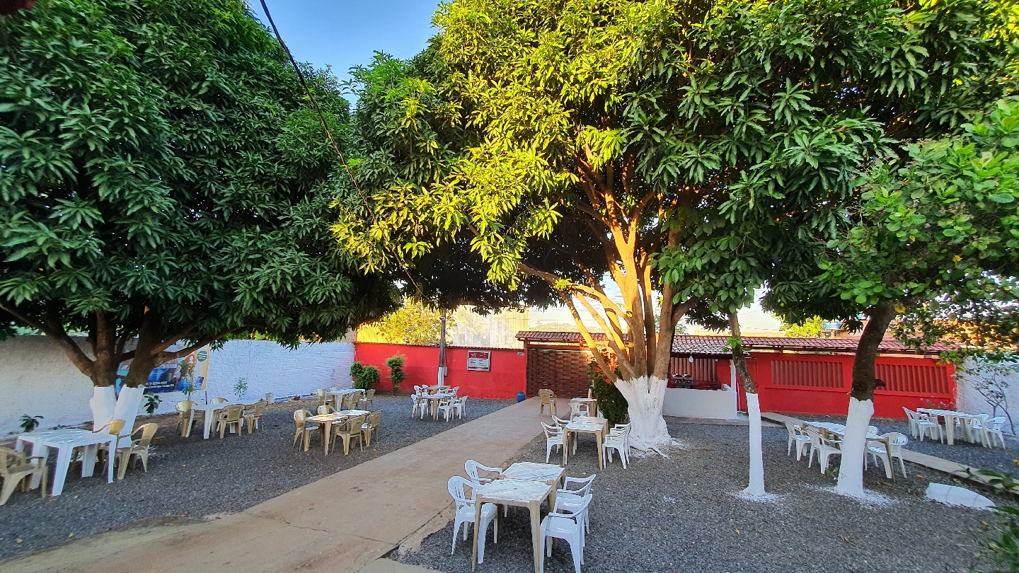Área ao ar livre com mesas na sombra de uma árvore durante o dia