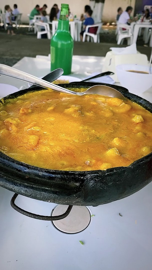 Moqueca dourada e fumegante servida num tacho de ferro