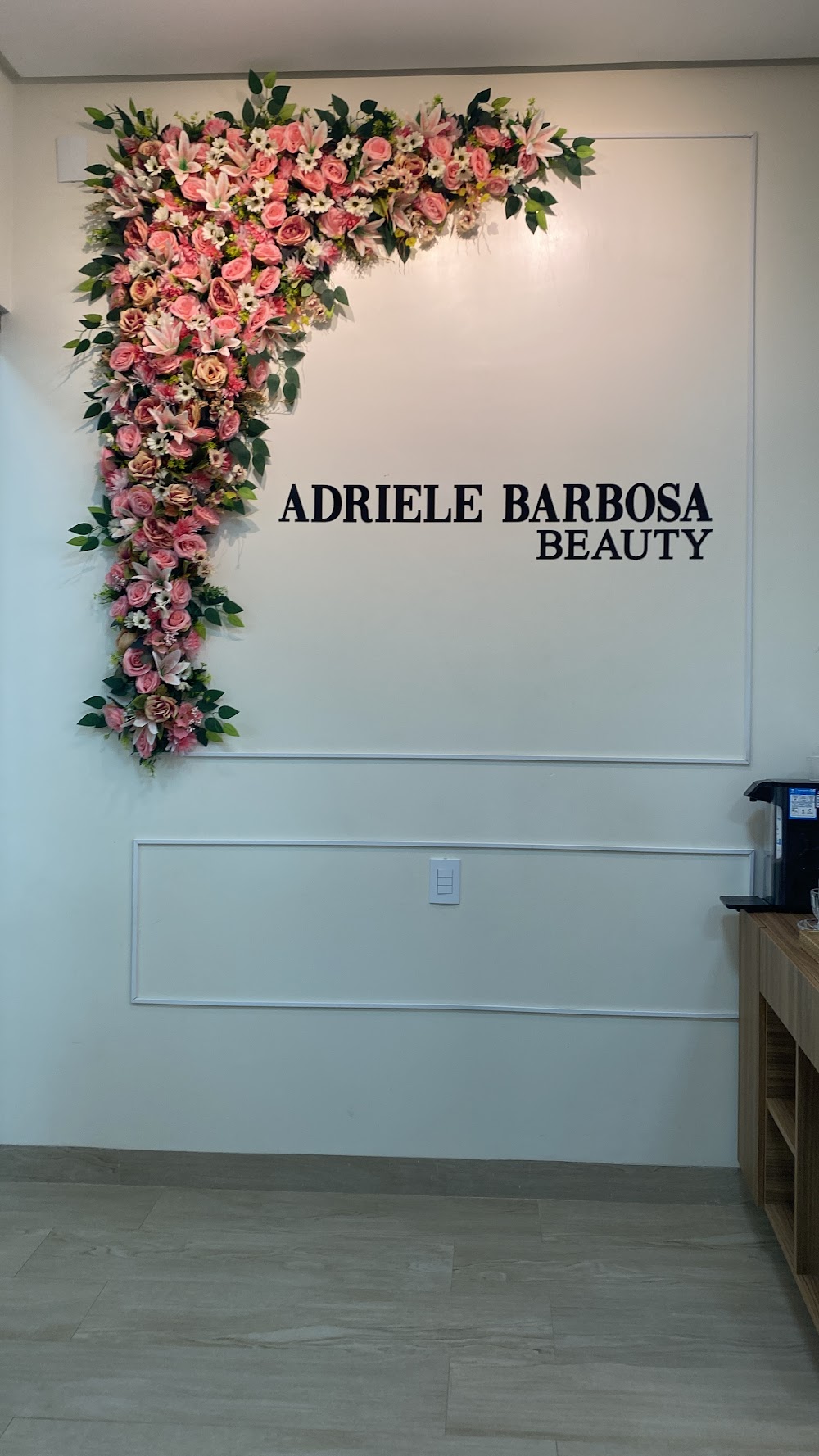 Recepção da Adriele Barbosa Beauty Boutique com o nome da marca na parede clara e um arranjo de flores em tons de rosa e coral