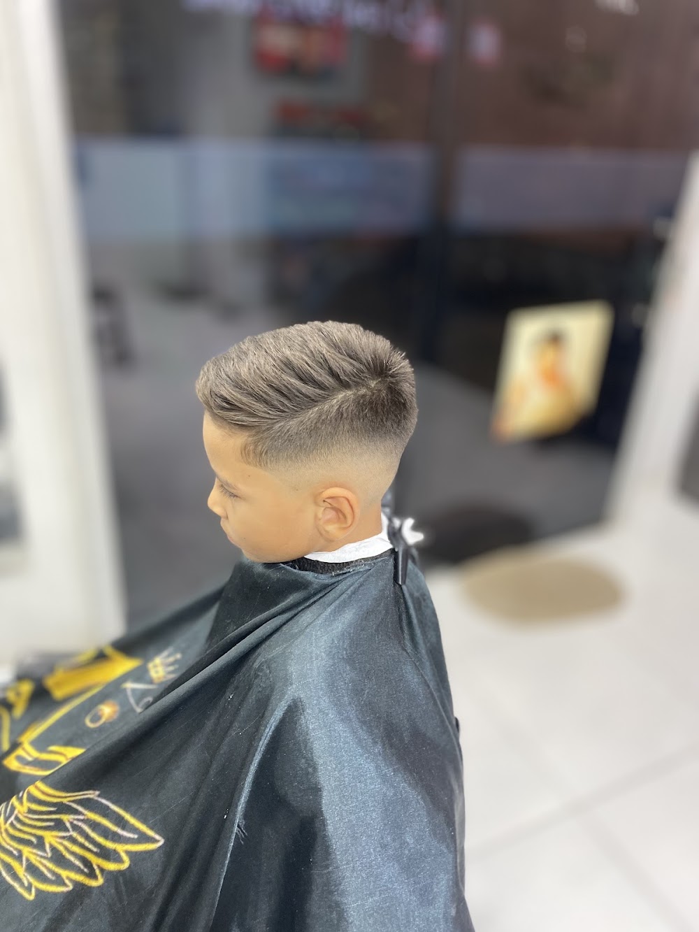 Criança com corte degradê feito na Barbearia Marcos, usando a capa preta com bordado dourado da barbearia