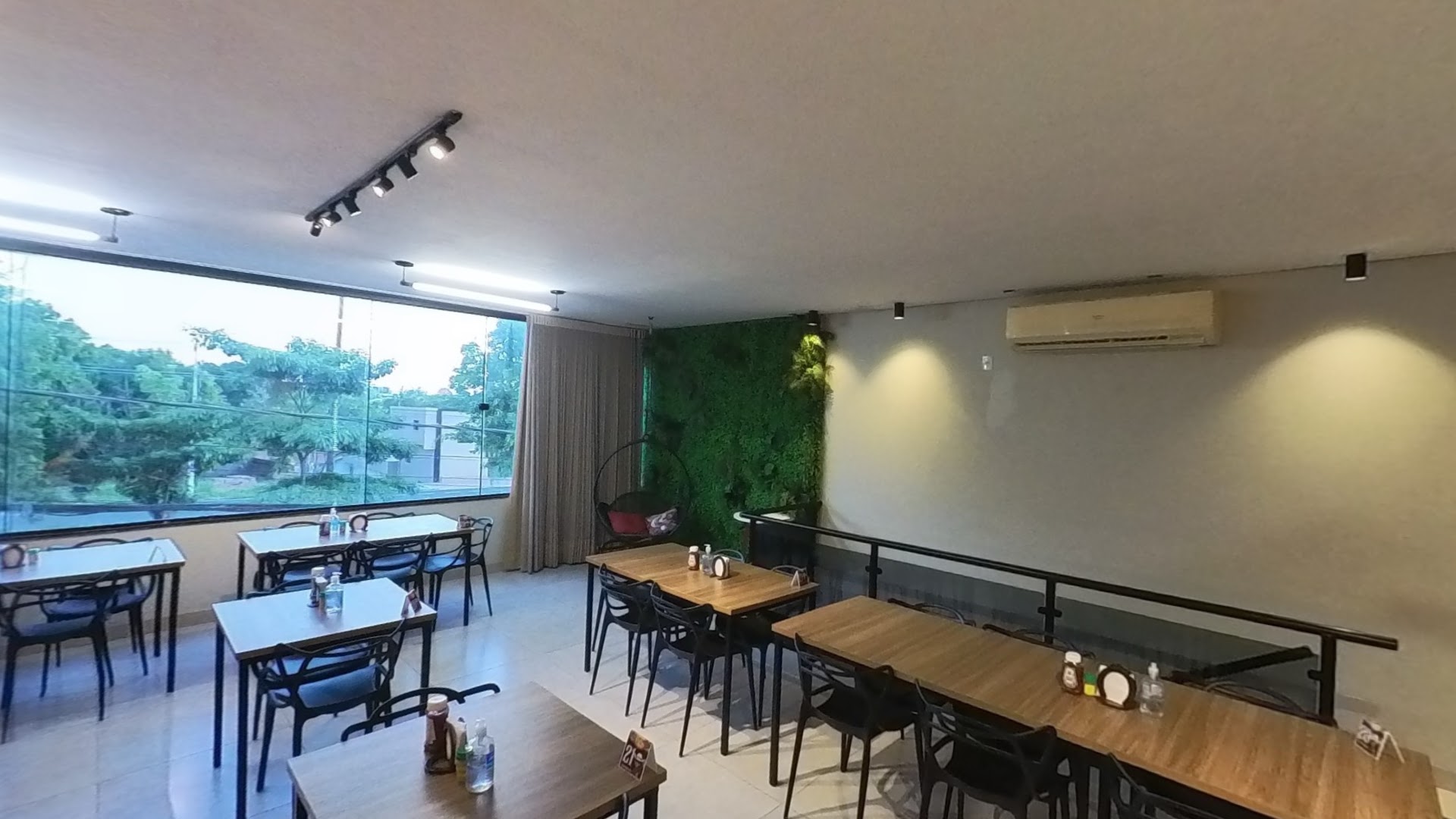 Interior moderno com parede verde, mesas de madeira e iluminação aconchegante