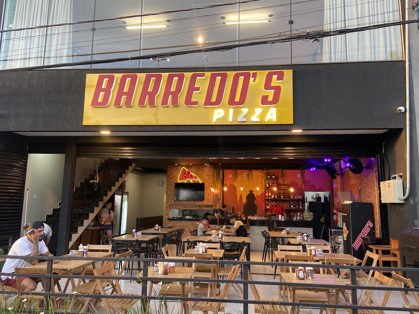 Fachada iluminada da Barredo's Pizza com o salão aberto e mesas na calçada