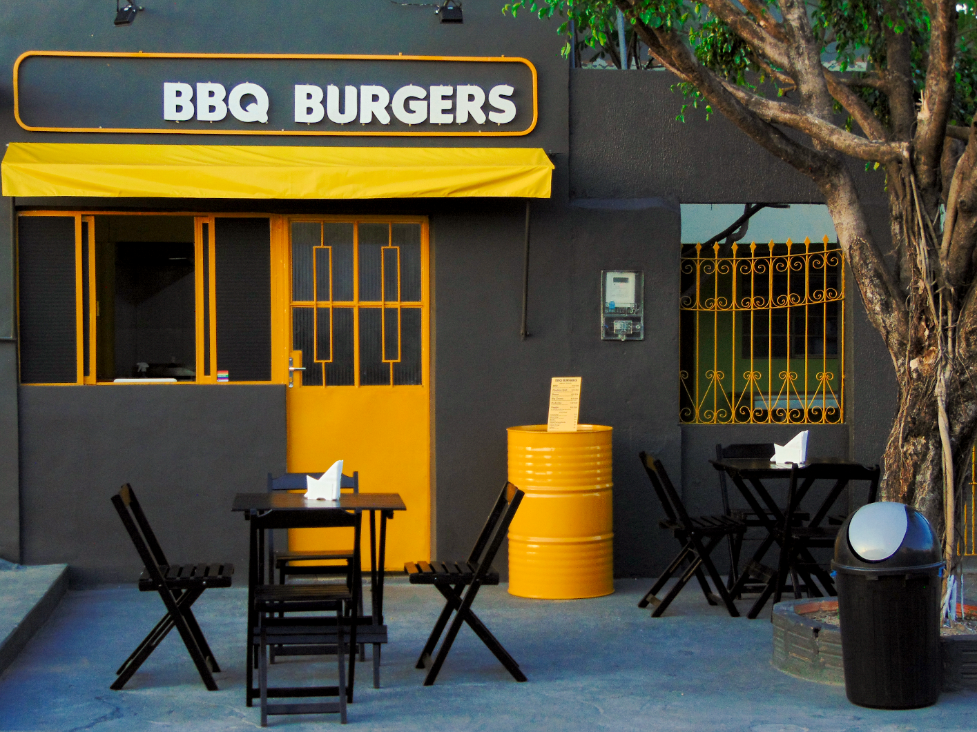 Fachada amarela BBQ Burgers com mesas na área externa