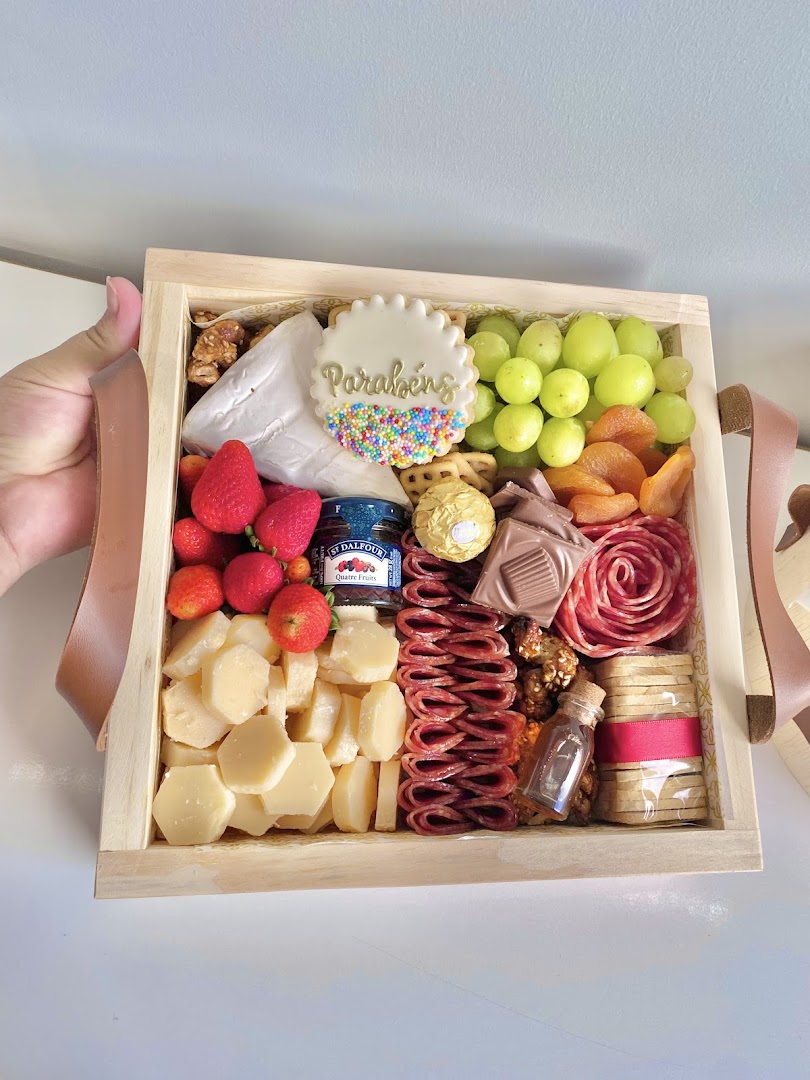 Box de café da manhã farto com uvas, chocolates, queijos em formato de coração, frutas e uma flor