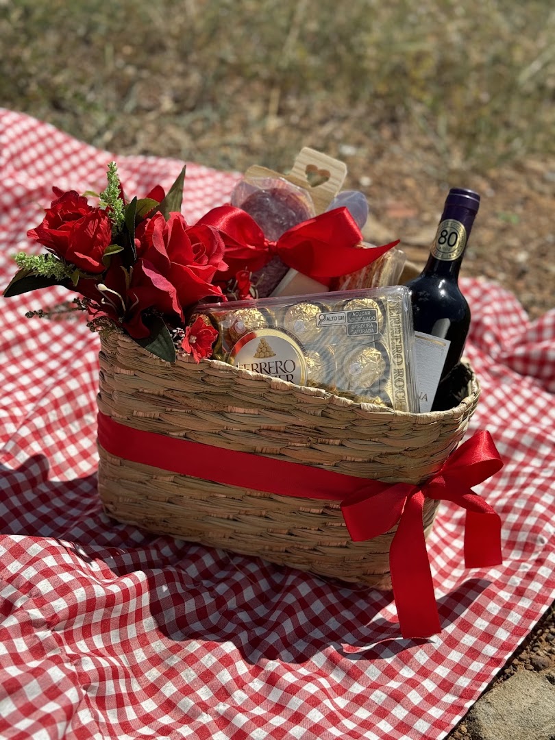 Cesta rústica com vinho, flores vermelhas e chocolates sobre toalha xadrez