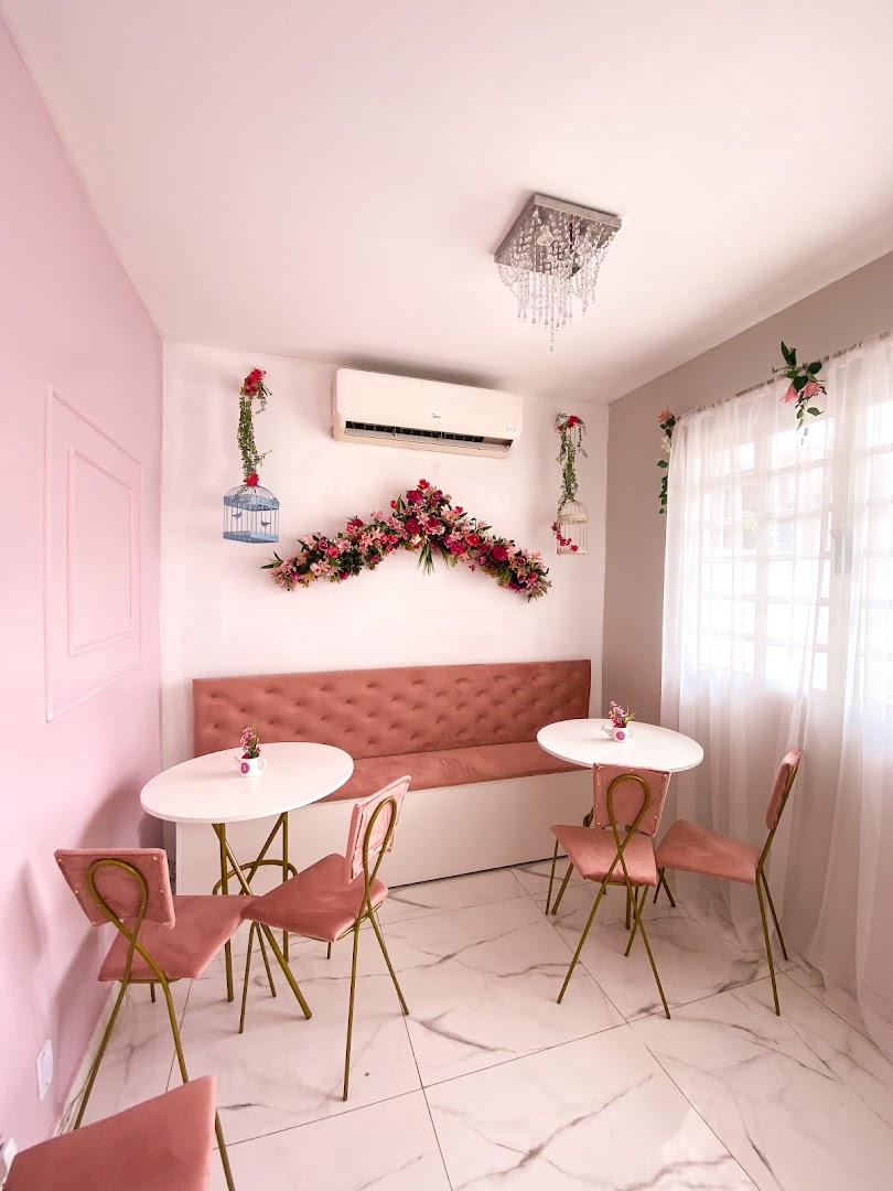 Salão em tons de rosa com poltrona aveludada, mesinhas brancas e lustre