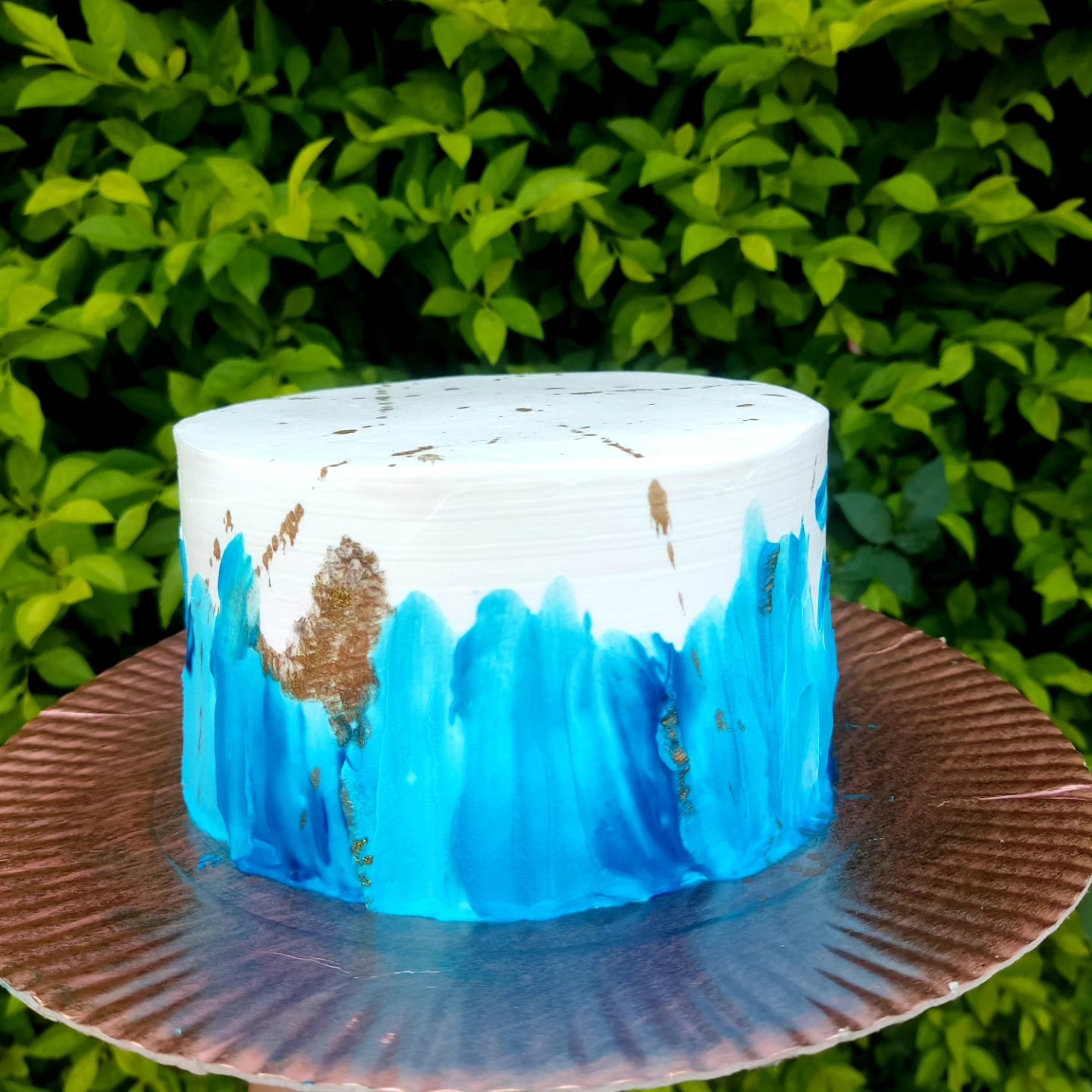 Bolo branco com pintura azul em aquarela e detalhes dourados