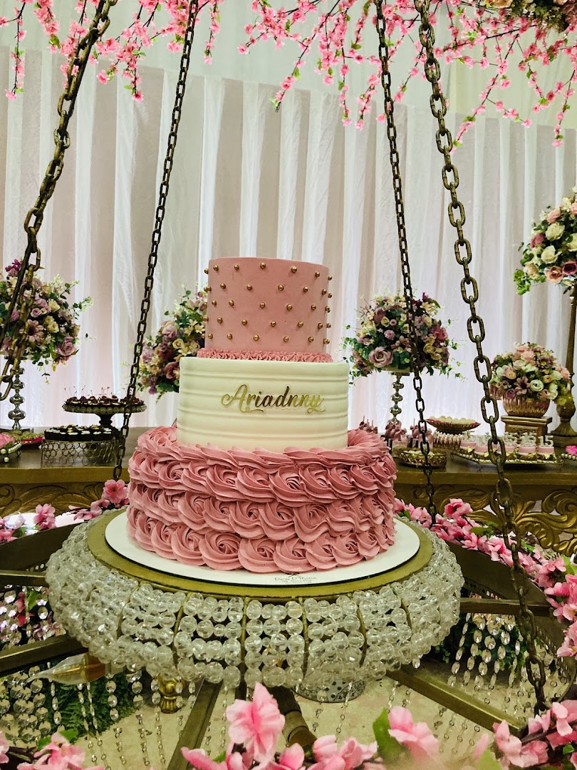 Bolo de três andares em rosa e dourado sobre suporte de festa