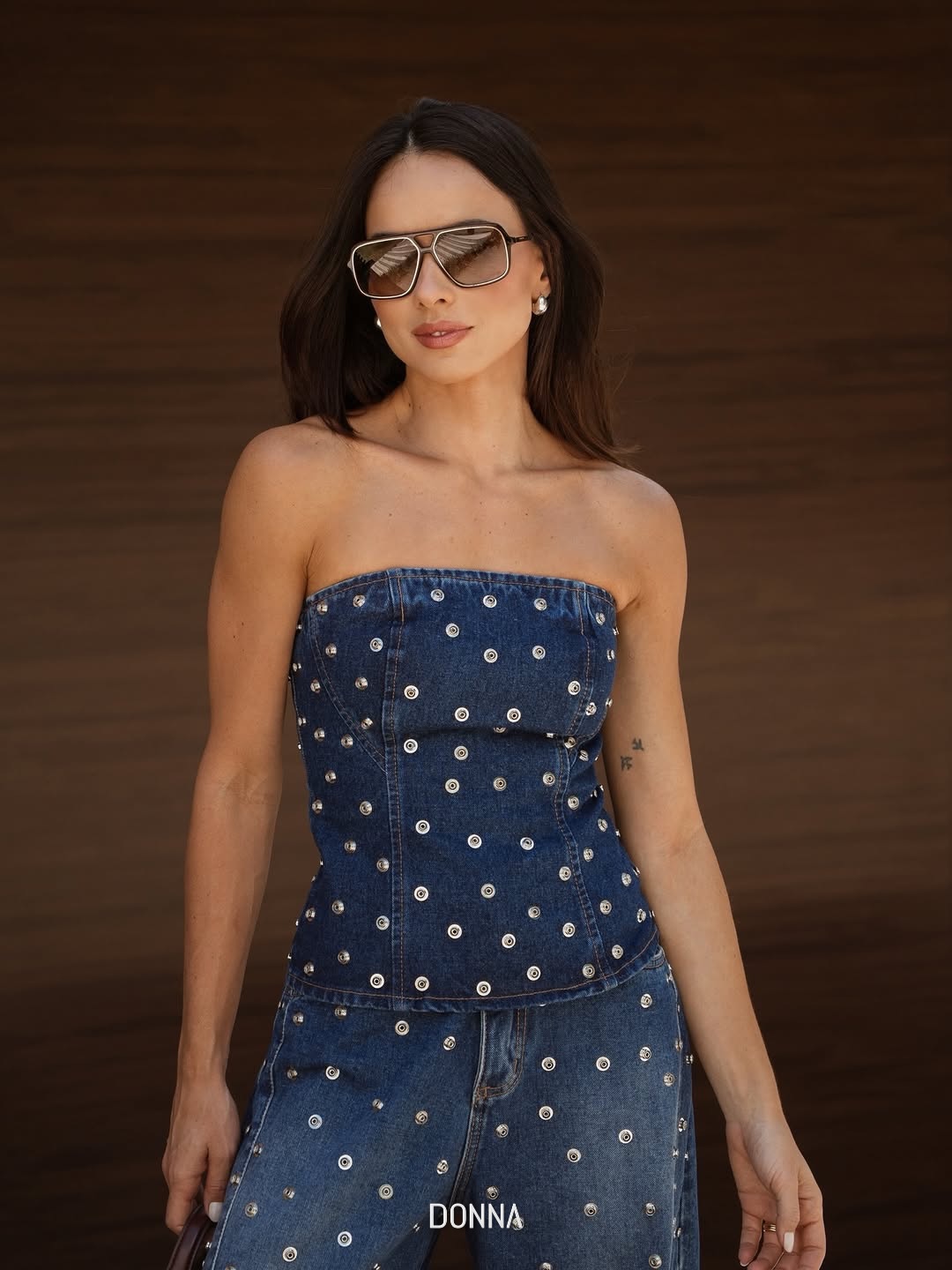 Modelo em conjunto jeans com tachas prateadas e óculos de sol