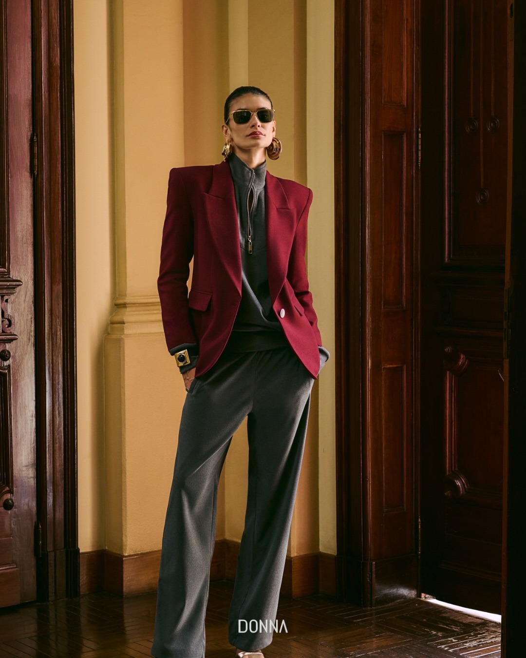 Modelo em blazer bord&ocirc;, blusa cinza e cal&ccedil;a de alfaiataria, entre portas de madeira