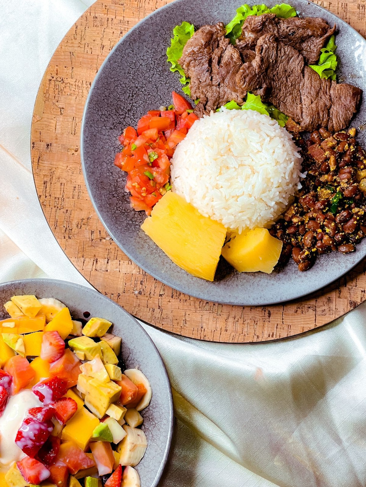 Prato com arroz, carne, feijão e abacaxi ao lado de salada de frutas
