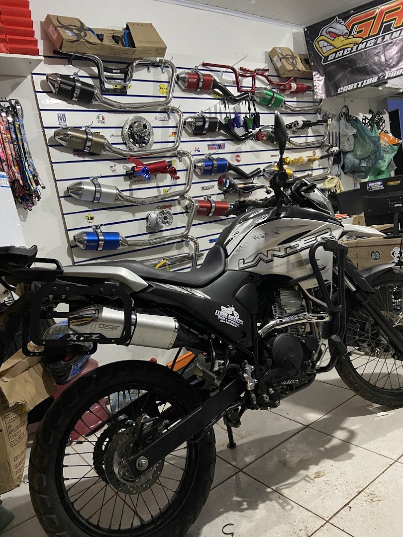 Moto branca dentro da loja com parede de escapamentos ao fundo