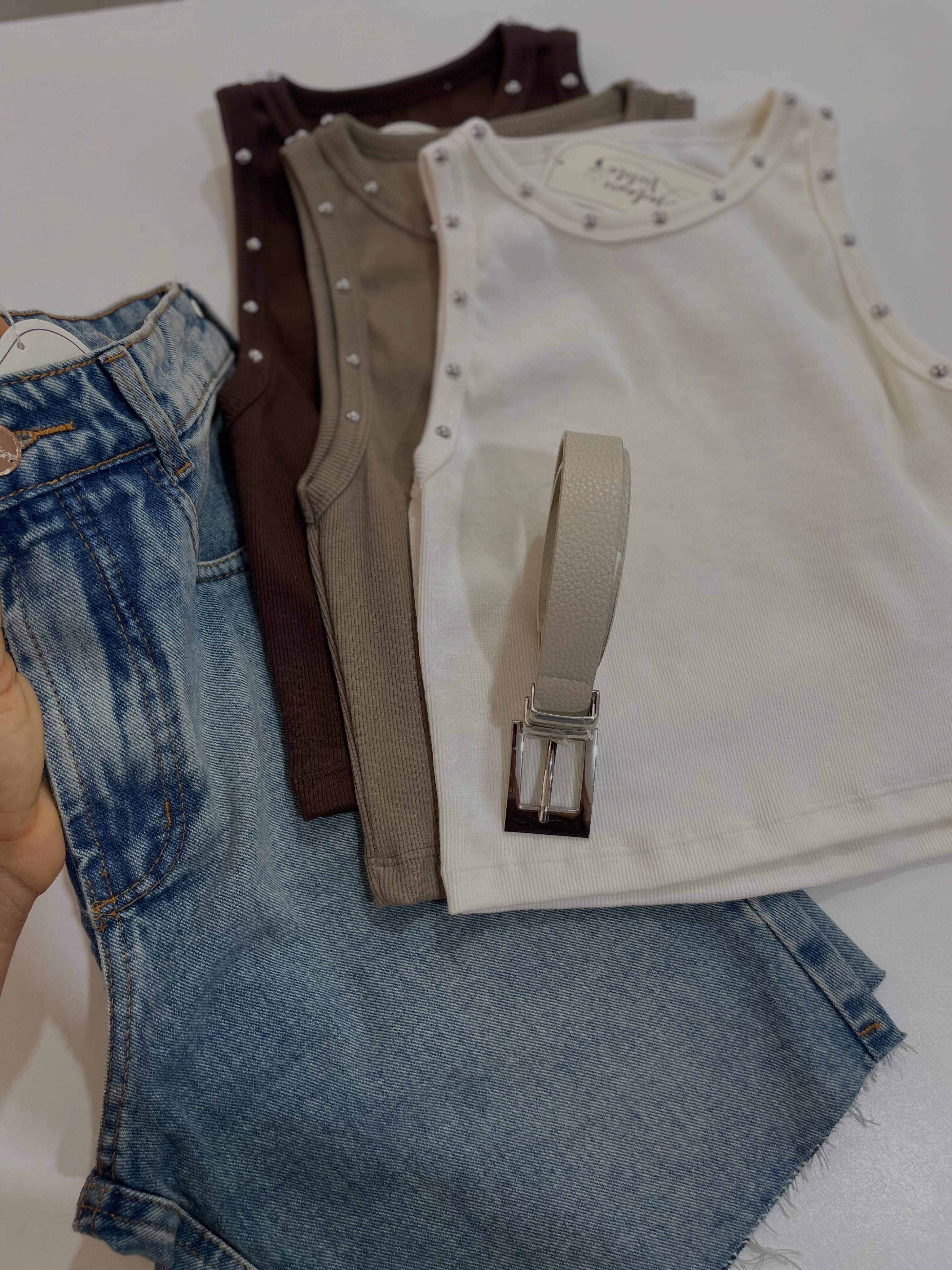 Flatlay de calça jeans com cinto, tops e acessórios