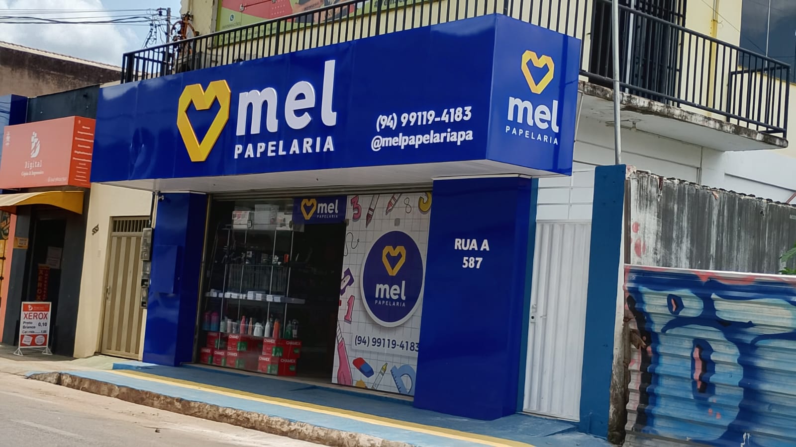 Fachada azul da Mel Papelaria com o logo de cora&ccedil;&atilde;o amarelo