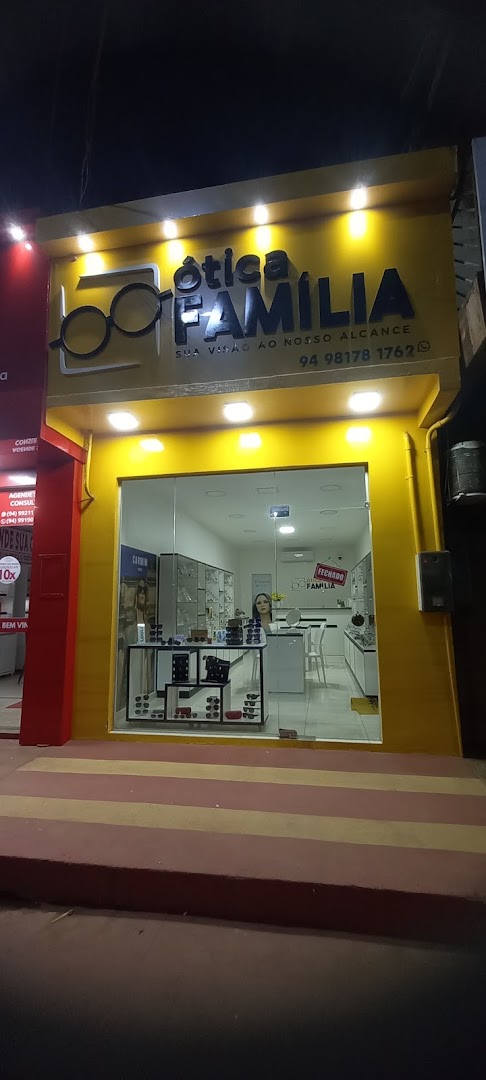 Interior iluminado da Ótica Família visto pela vitrine, com balcão e prateleiras de óculos