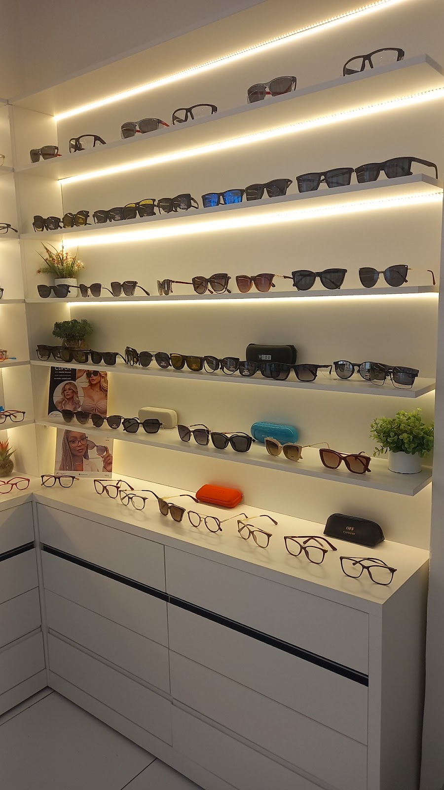 Prateleiras iluminadas da Ótica família com óculos de sol e de grau expostos