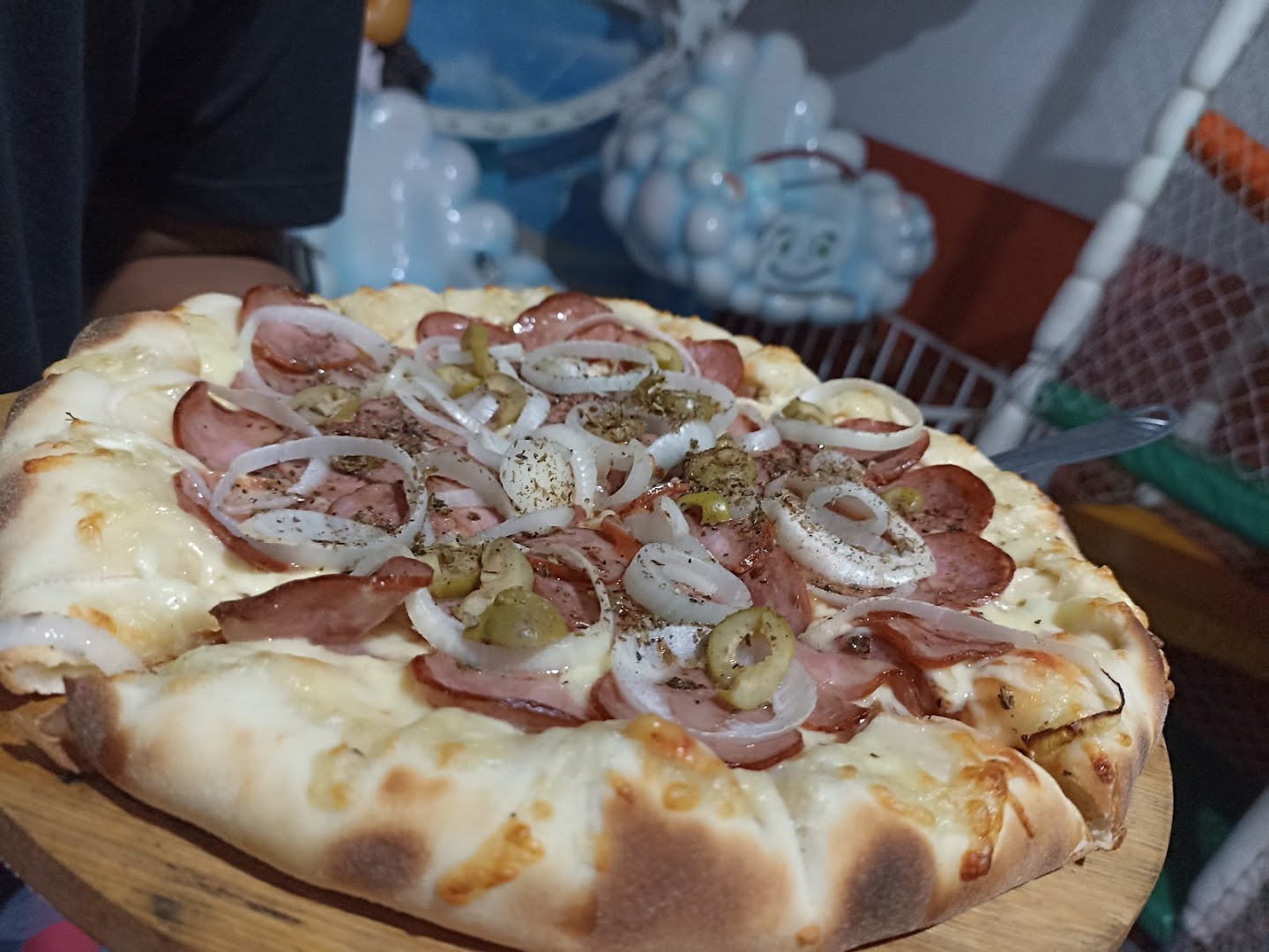 Pizza artesanal de calabresa com cebola, bem recheada, servida na tábua de madeira