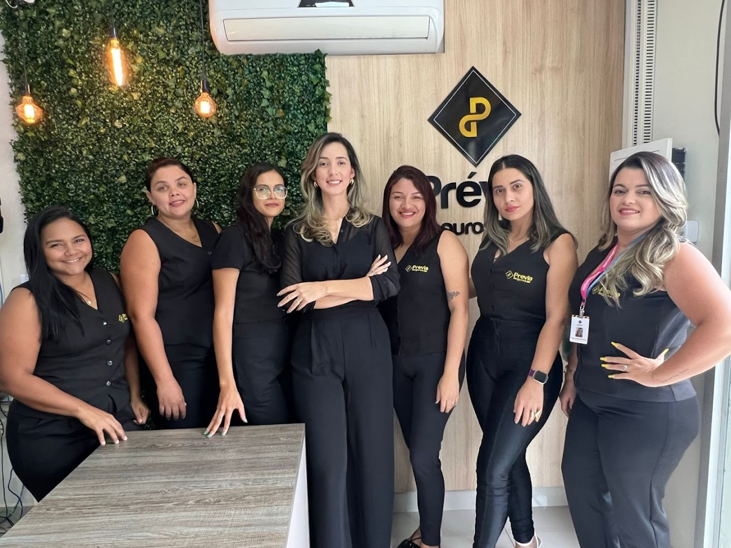 Equipe de seis corretoras da Prévia Seguros, todas de preto, no escritório