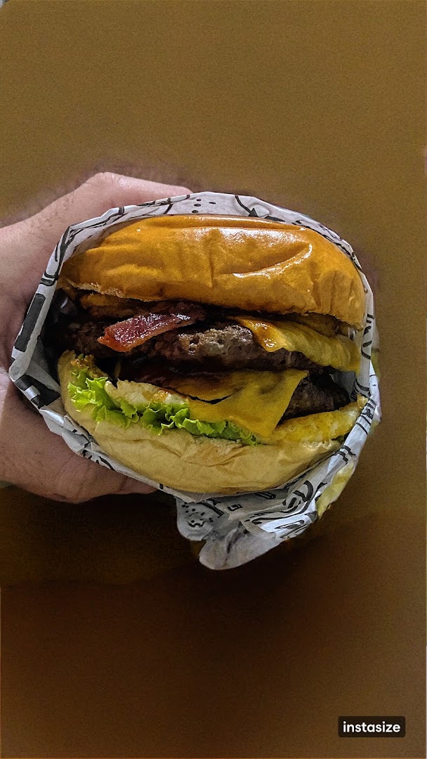 Hambúrguer de bacon segurado na mão, embrulhado no papel da casa