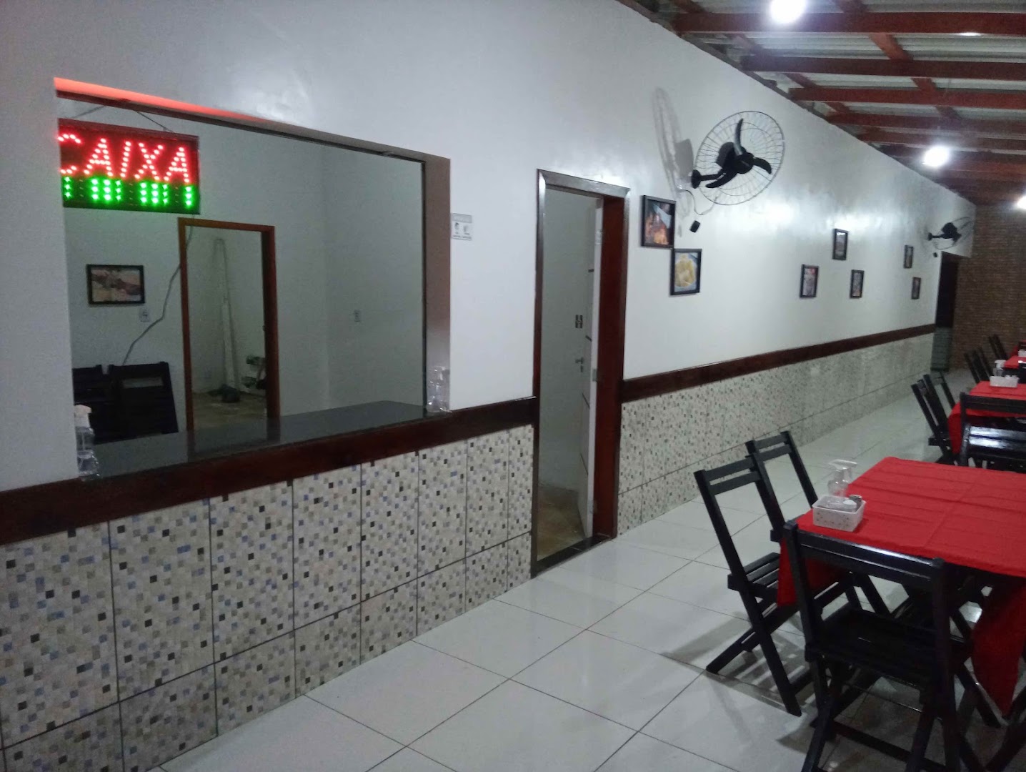 Salão interno do restaurante com mesas de toalha vermelha e cadeiras