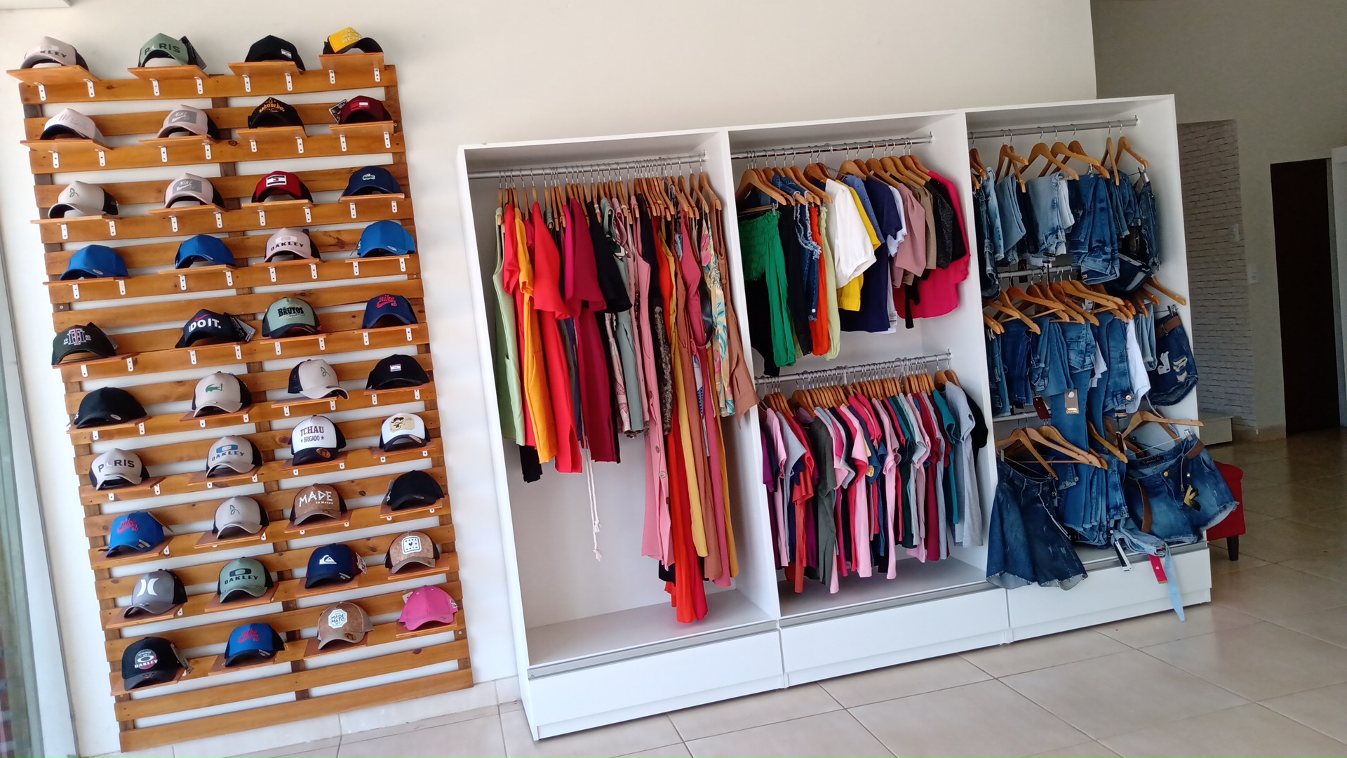 Arara de roupas coloridas variadas e expositor de bones na loja Ruiva Morena