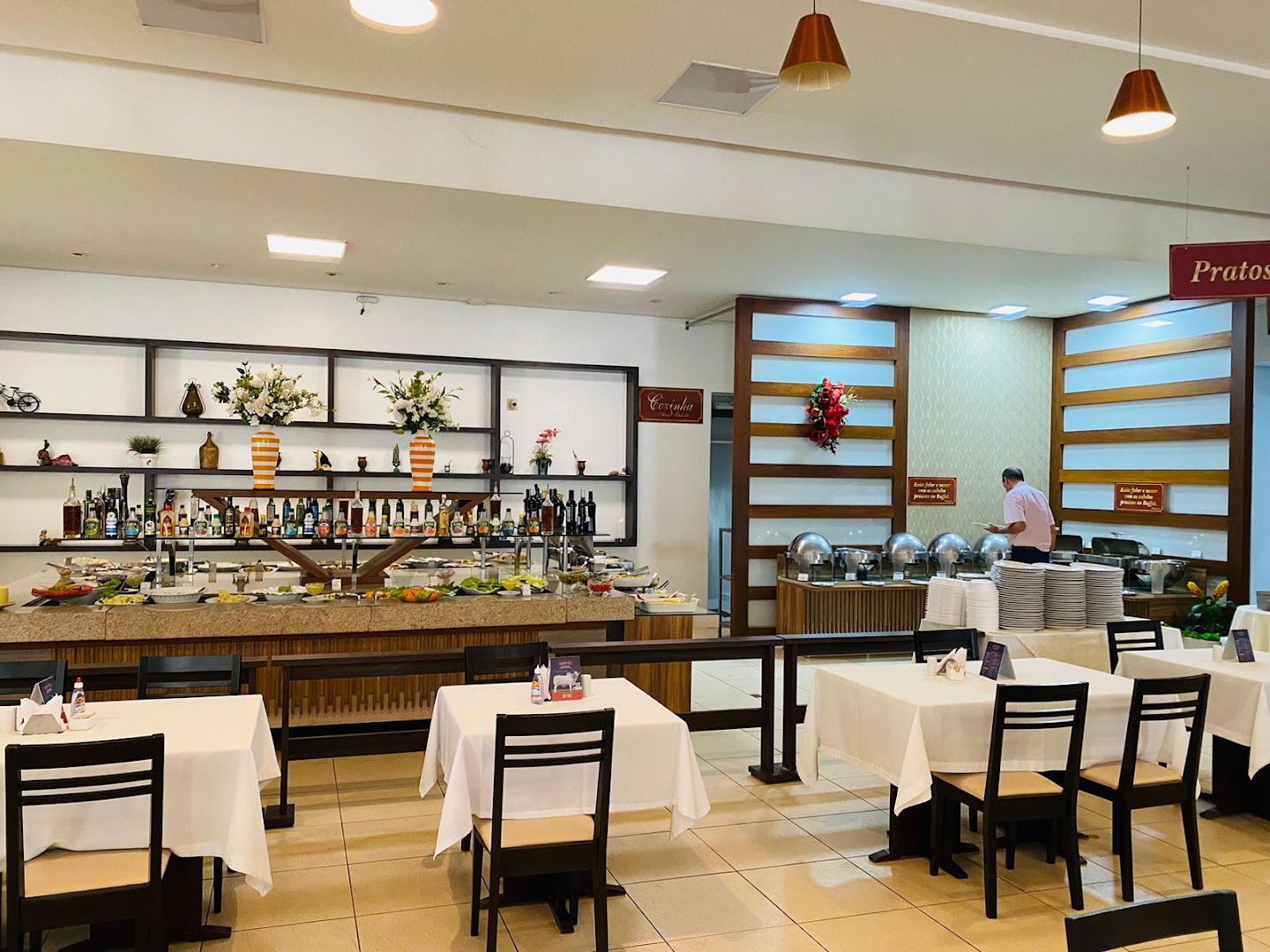 Salão com o buffet ao fundo e mesas com toalha branca