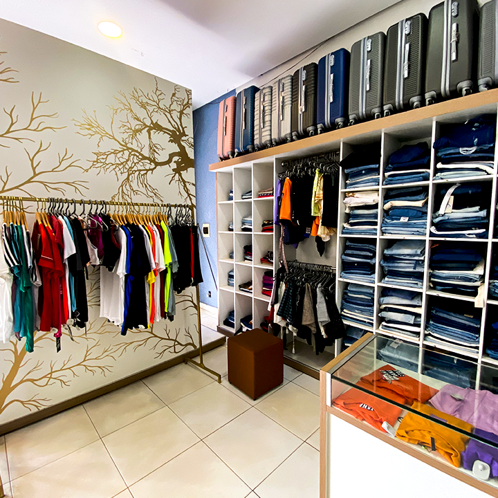 Interior amplo e claro da loja, com araras de roupa e um painel decorativo de árvore ao fundo